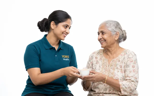 A caregiver handing an older woman a cup of tea